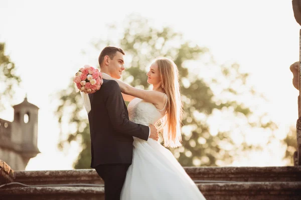 Beautiful romantic wedding couple of newlyweds hugging near old castle on sunset — Stock Photo, Image