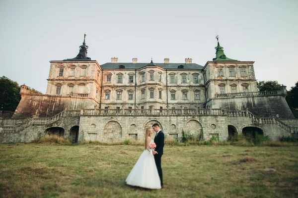 Krásné romantické svatební pár, ženich a nevěsta objímání poblíž starého hradu na západ slunce — Stock fotografie