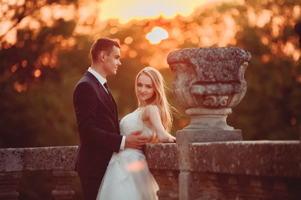 Hermosa pareja romántica de boda, novio y novia abrazándose cerca del viejo castillo en la puesta del sol — Foto de Stock