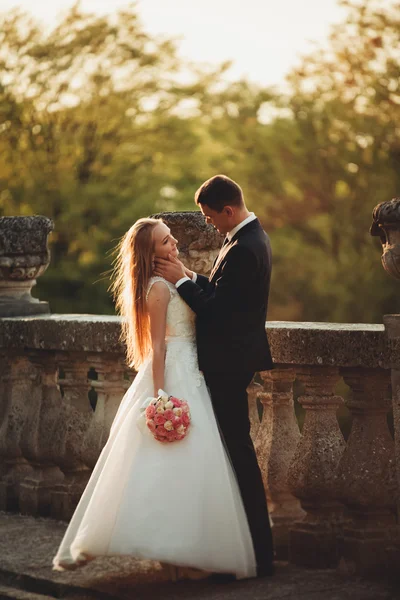 Beau couple de mariage romantique de jeunes mariés étreignant près du vieux château au coucher du soleil — Photo