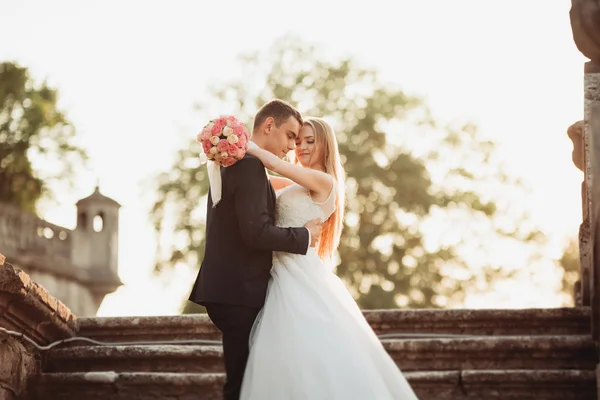 Beau couple de mariage romantique de jeunes mariés étreignant près du vieux château au coucher du soleil — Photo