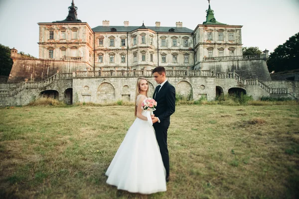 Krásné romantické svatební pár, ženich a nevěsta objímání poblíž starého hradu na západ slunce — Stock fotografie