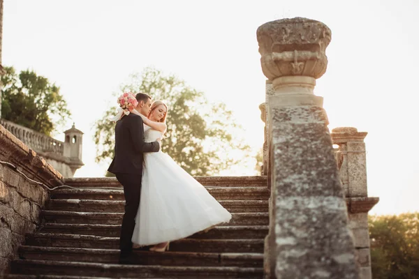 Beau couple de mariage romantique de jeunes mariés étreignant près du vieux château au coucher du soleil — Photo