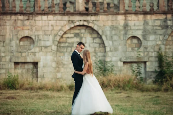 Beau couple de mariage romantique de jeunes mariés étreignant près du vieux château au coucher du soleil — Photo