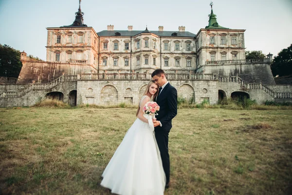 Schönes romantisches Hochzeitspaar, Bräutigam und Braut umarmen sich bei Sonnenuntergang in der Nähe des alten Schlosses — Stockfoto