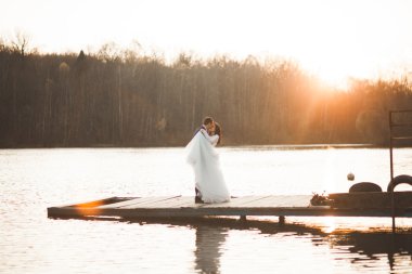 Zarif güzel düğün çifti bir göl kenarında günbatımında poz