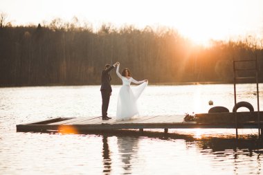 Zarif güzel düğün çifti bir göl kenarında günbatımında poz