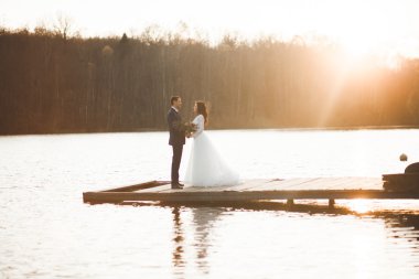 Zarif güzel düğün çifti bir göl kenarında günbatımında poz