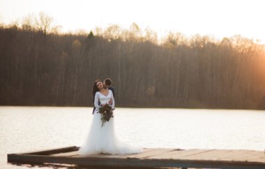 Zarif güzel düğün çifti bir göl kenarında günbatımında poz