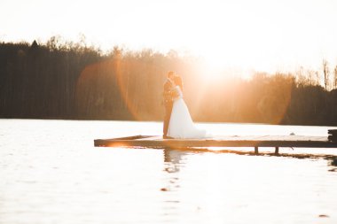 Zarif güzel düğün çifti bir göl kenarında günbatımında poz