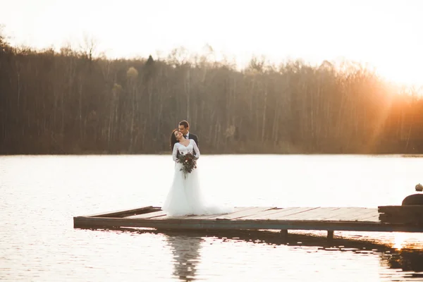 Elegante bella coppia di nozze in posa vicino a un lago al tramonto — Foto Stock