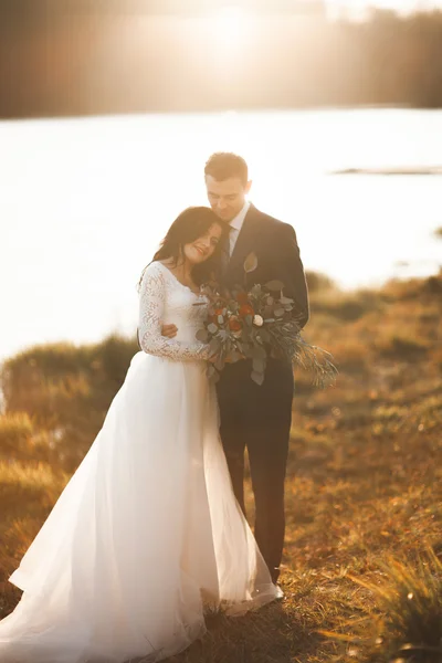 Elegante mooie bruidspaar poseren in de buurt van een meer bij zonsondergang — Stockfoto