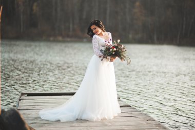 Orman ve göl poz buket tutan şık elbiseli güzel esmer gelin