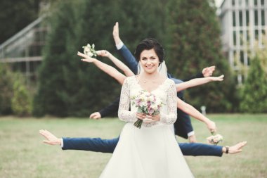 Zarif beyaz elbiseli güzel esmer gelin elinde buket ile güzel ağaçlar poz veriyor.