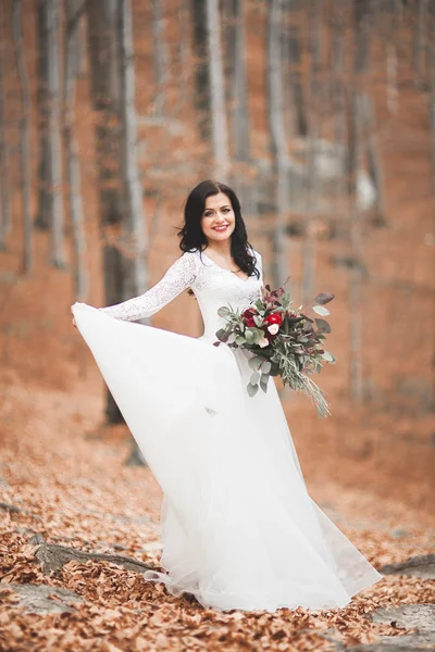 Hermosa novia morena en vestido elegante celebración de ramo posando cerca del bosque y el lago — Foto de Stock
