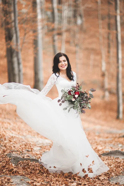 Prachtige brunette bruid in elegante jurk bedrijf boeket poseren in de buurt van bos en meer — Stockfoto