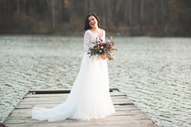 Orman ve göl poz buket tutan şık elbiseli güzel esmer gelin