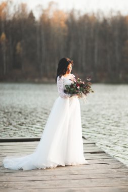 Orman ve göl poz buket tutan şık elbiseli güzel esmer gelin
