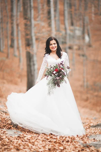 Wunderschöne brünette Braut im eleganten Kleid mit Blumenstrauß posiert in der Nähe von Wald und See — Stockfoto