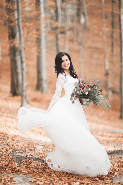 Wunderschöne brünette Braut im eleganten Kleid mit Blumenstrauß posiert in der Nähe von Wald und See — Stockfoto