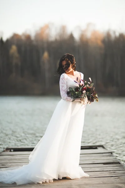 森と湖に近いポーズの花束を持ってエレガントなドレスにゴージャスなブルネット花嫁 — ストック写真