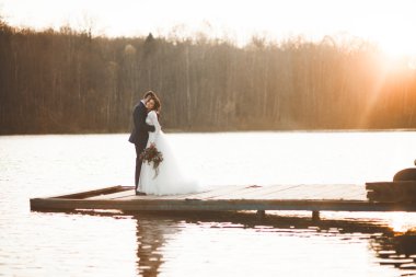 Zarif güzel düğün çifti bir göl kenarında günbatımında poz