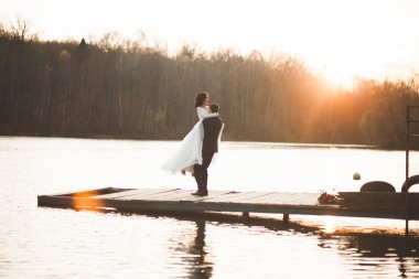 Zarif güzel düğün çifti bir göl kenarında günbatımında poz