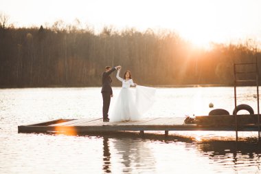 Zarif güzel düğün çifti bir göl kenarında günbatımında poz