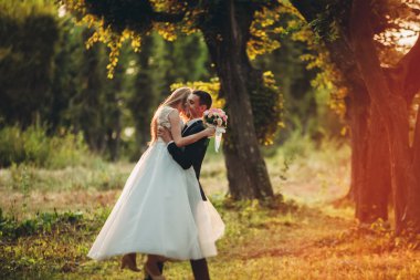 Güzel romantik bir çift yeni evliler gün batımında parkta sarılıyorlar.