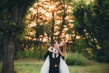 Güzel romantik bir çift yeni evliler gün batımında parkta sarılıyorlar.