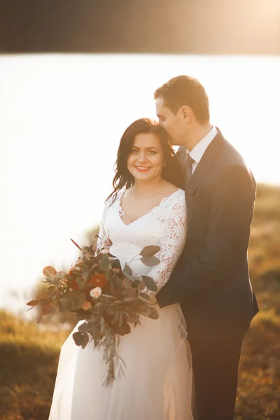 Elegante bella coppia di nozze in posa vicino a un lago al tramonto — Foto Stock