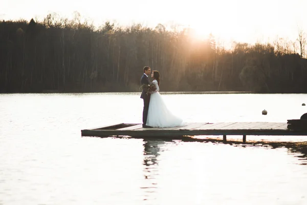 Elegante hermosa pareja de boda posando cerca de un lago al atardecer — Foto de Stock