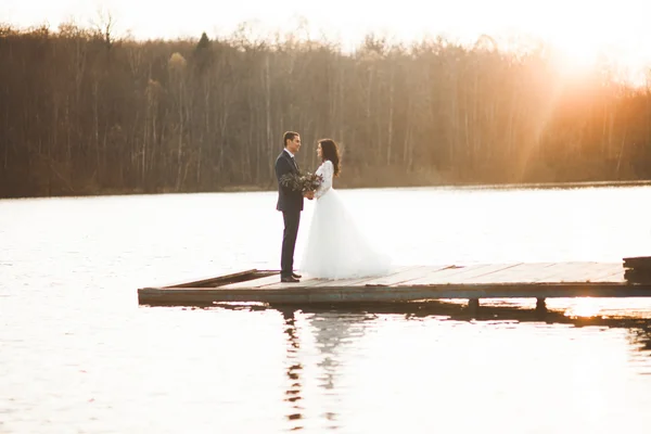 Elegáns gyönyörű esküvői pár jelentő közelében egy tó naplementekor — Stock Fotó