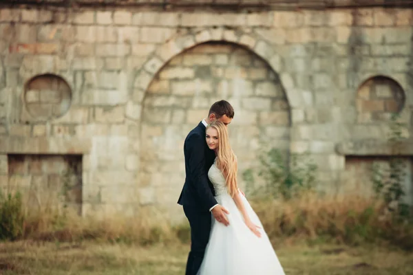 Hermosa pareja romántica de recién casados abrazándose cerca del viejo castillo en la puesta del sol — Foto de Stock