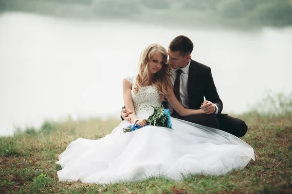 Happy wedding couple sitting on the ground near lake — Stock Photo, Image