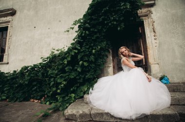 Güzel genç sarışın gelin gelin buketi merdiven arka plan güzel bitkiler üzerinde oturan ile