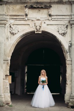 Güzel genç sarışın gelin gelin buketi ile antik kemer üzerinde duruyor