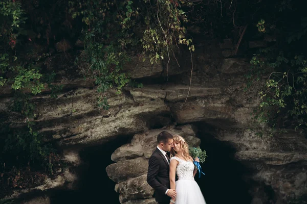 古代の城に近い洞窟のハグとキスを背景の豪華な植物に高級結婚式のカップル — ストック写真