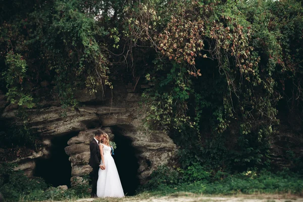 Pareja de boda de lujo abrazos y besos en el fondo hermosas plantas, cueva cerca del antiguo castillo —  Fotos de Stock