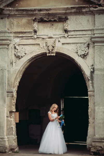 Güzel genç sarışın gelin gelin buketi ile antik kemer üzerinde duruyor
