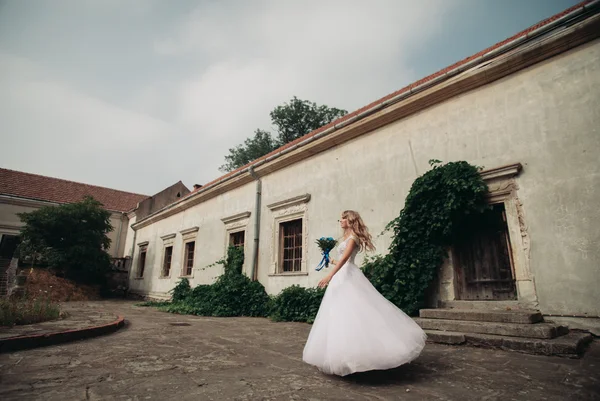 Schöne junge blonde Braut mit Brautstrauß tanzen auf dem Hintergrund wunderschöne Pflanzen — Stockfoto
