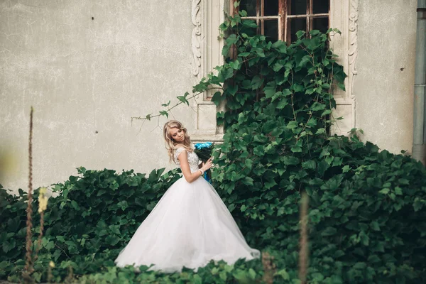 Joven novia rubia de lujo con ramo de novia posa en el fondo hermosas plantas — Foto de Stock