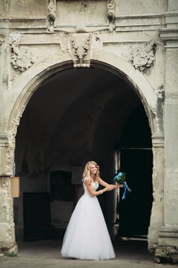 Güzel genç sarışın gelin gelin buketi ile antik kemer üzerinde duruyor