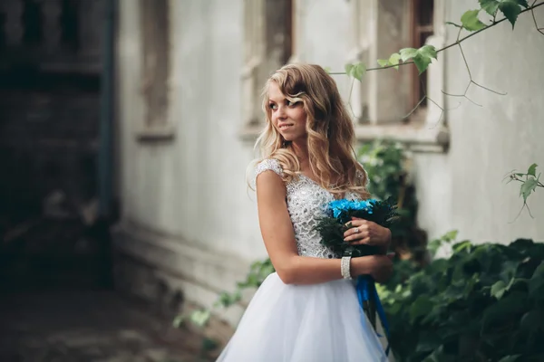 Lyxiga ung blond brud med brudbukett poser på bakgrunden vackra växter — Stockfoto