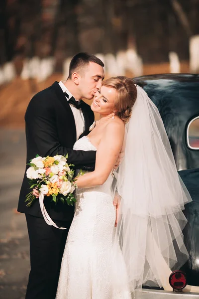 Stijlvolle bruidspaar, bruid, bruidegom zoenen en knuffelen in de buurt van retro auto in de herfst — Stockfoto