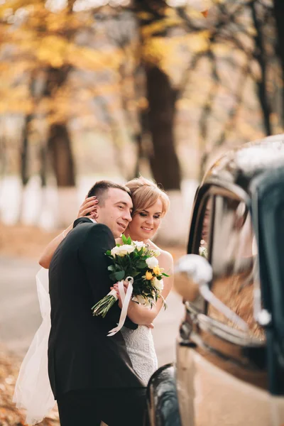 Elegante pareja de boda, novia, novio besándose y abrazándose cerca de coche retro en otoño —  Fotos de Stock