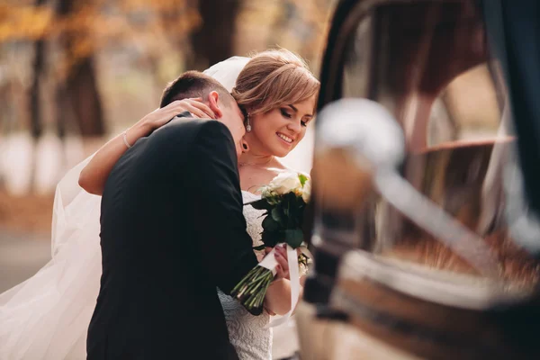 Stilvolles Hochzeitspaar, Braut, Bräutigam küssen und umarmen sich im Herbst in der Nähe von Retro-Autos — Stockfoto