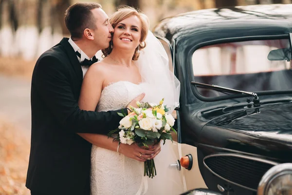 Stilvolles Hochzeitspaar, Braut, Bräutigam küssen und umarmen sich im Herbst in der Nähe von Retro-Autos — Stockfoto