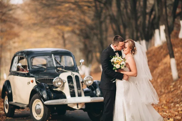 Stilvolles Hochzeitspaar, Braut, Bräutigam küssen und umarmen sich im Herbst in der Nähe von Retro-Autos — Stockfoto