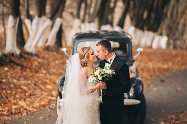 Elegantní Svatební pár, nevěsta, ženich, líbání a objímání poblíž retro auto na podzim — Stock fotografie